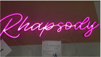 Lit up pink LED light that reads Rhapsody laying on factory floor getting ready for shipment